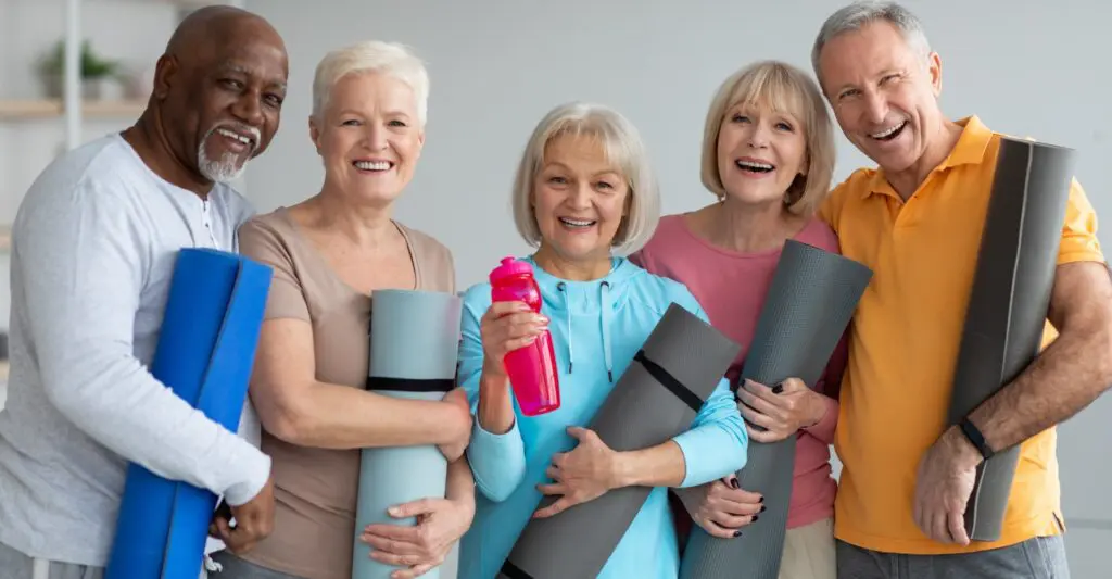 Diverse senior group holding fitness equipment, smiling and staying active together indoors.