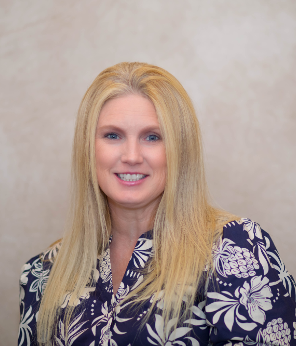Blonde woman smiling wearing blue and white floral blouse against beige background